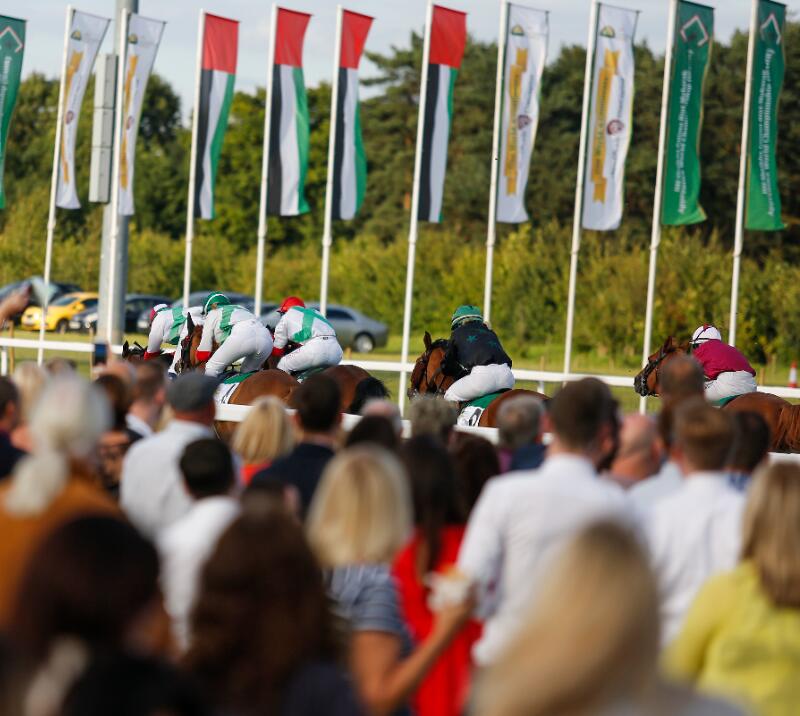 Crowds watching jockeys race past.
