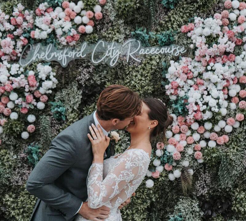 Couple kissing in front of live wall full of flowers.